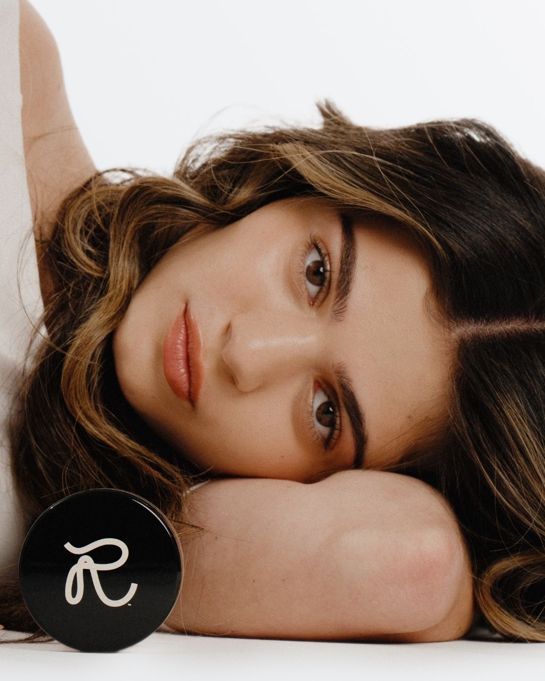 Woman lying down with a close-up of her face, featuring a brand logo in the corner.