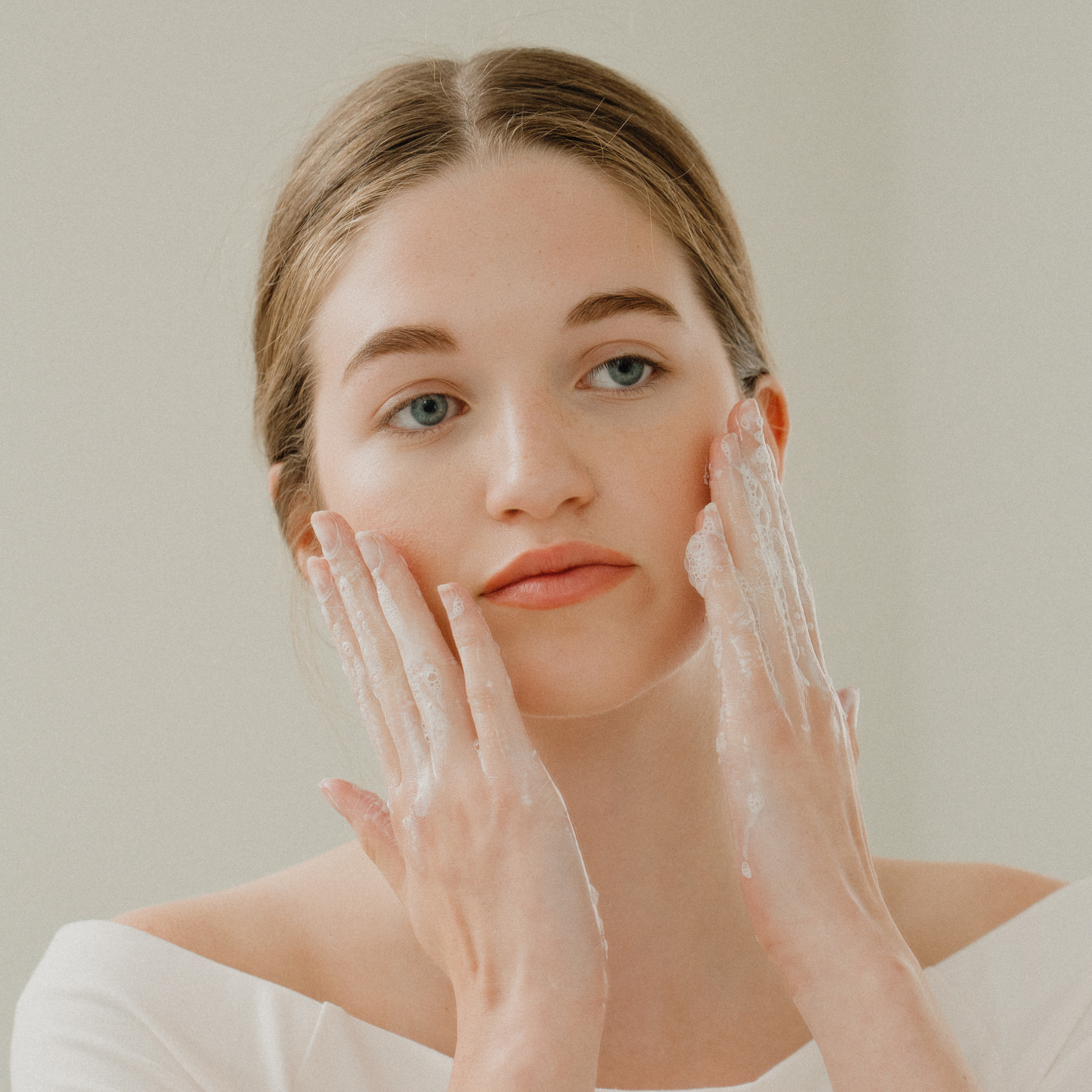 Woman applying a skincare product to her face with a neutral background