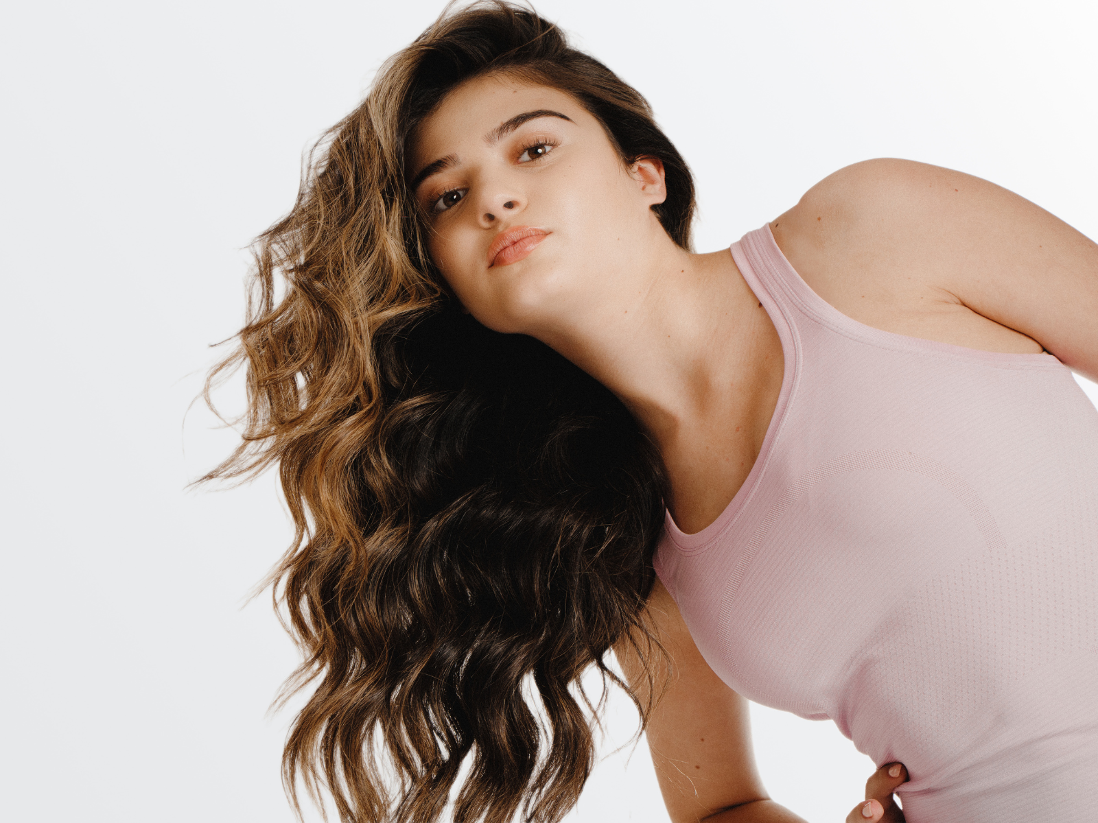 Woman with wavy hair wearing a pink tank top against a white background